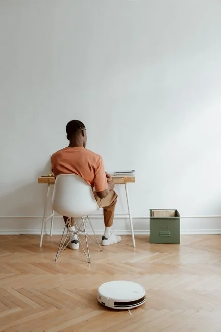 who-we-are Intérieur élégant avec des cartons de déménagement étiquetés Kitchen et Office sur une table en bois, entourée de plantes d’intérieur.